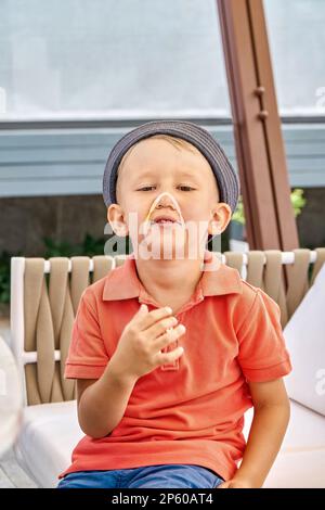 Kleinkinder mit panama Grimaces und Gummiarmband am Gesichtsausschnitt. Das verspielte kleine Kind hat Spaß daran, in die Kamera zu schauen Stockfoto