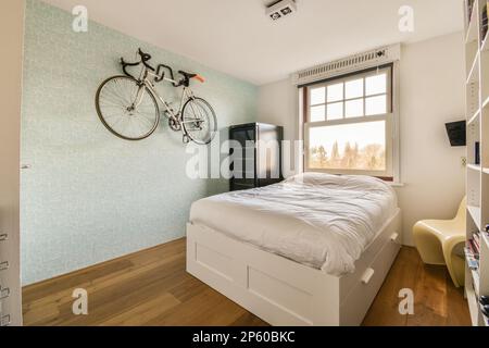 Ein Schlafzimmer mit einem Fahrrad an der Wand darüber und einem Bett, das zu einem Kopfteil gemacht wurde Stockfoto