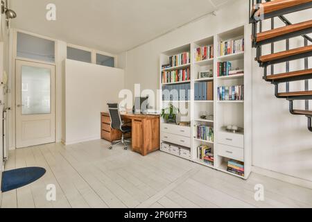 Amsterdam, Niederlande - 10. April 2021: Ein Heimbüro mit Bücherschellen an der Wand und Treppen bis zur zweiten Etage in einem Apartment Stockfoto