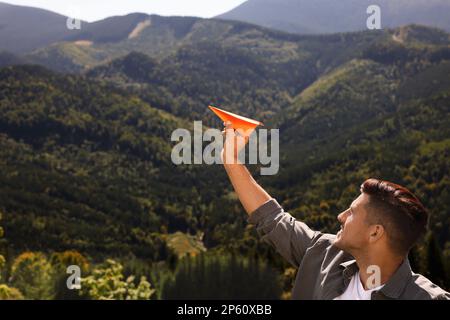 Ein Mann, der ein Papierflugzeug in die Berge wirft, an einem sonnigen Tag. Platz für Text Stockfoto