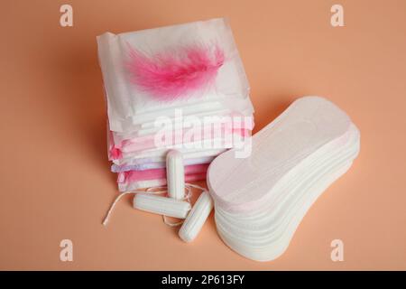Menstruationsmatten mit rosafarbener Feder und anderen Periodenprodukten auf blassorangefarbenem Hintergrund Stockfoto
