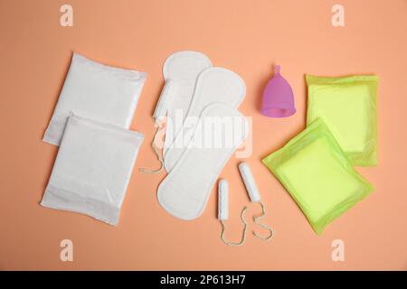 Menstruationseinlagen und andere Periodenprodukte auf blassorangefarbenem Hintergrund, flach liegend Stockfoto