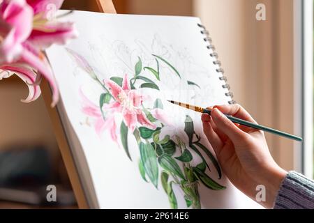 Ein junges Mädchen malt Stille Leben mit Blumen, lila Lilien, mit Aquarellfarben auf der Staffelei zu Hause Stockfoto