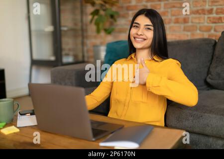 Eine positive mexikanische Dame zeigte Daumen-hoch-Geste und benutzte einen Laptop, machte Hausaufgaben, empfahl eine Online-Schule Stockfoto