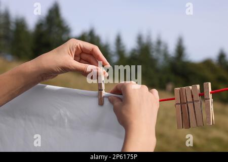 Eine Frau, die saubere Wäsche aufhängt, mit Wäscheklammern an der Wäscheleine draußen, Nahaufnahme Stockfoto