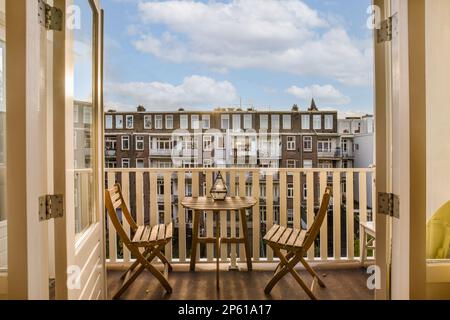 Ein Balkon mit zwei Stühlen und einem Tisch vor der Tür, der zu einer Außenterrasse führt Stockfoto