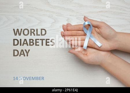 Weltdiabetestag. Frau mit hellblauem Farbband am Holztisch, Nahaufnahme Stockfoto