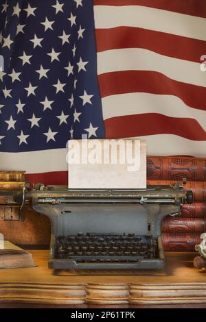 Ein alter Holzschreibtisch mit einer alten Schreibmaschine, die ein leeres Blatt Papier vor der US-Flagge hält Stockfoto