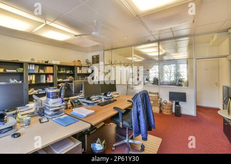 Ein Büro mit Schreibtischen, Computern und anderen Dingen auf dem Tisch vor dem Computerbildschirm ist offen Stockfoto