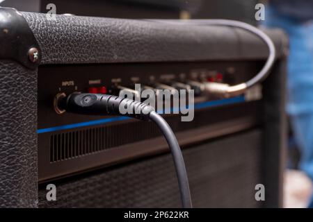 Klinke mit Kabel, das in einen schwarzen Gitarrenverstärker gesteckt wird Stockfoto