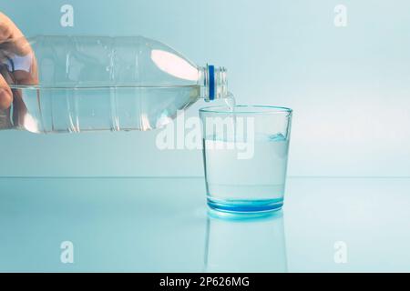 Gießen Wasser aus der Flasche ins Glas auf blauem Hintergrund Stockfoto