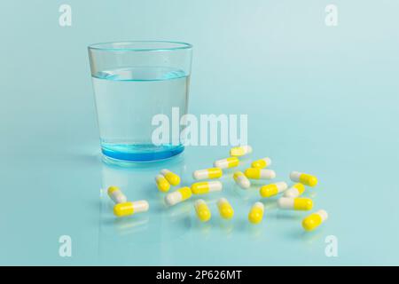 Wasserglas und weiße und gelbe Tabletten auf blauem Hintergrund. Gesundheit und Medizin. Speicherplatz kopieren. Stockfoto