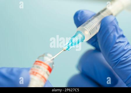 Makro einer hypodermischen Spritze oder Nadel, die mit mRNA-Impfstoff aus der Flasche vor blauem Hintergrund gefüllt wird Stockfoto