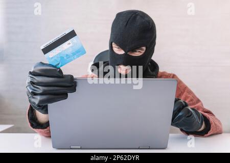 Diebe halten Kreditkarten mit einem Laptop, um Passwörter zu hacken. Konzepte der Cyberkriminalität. Ein männlicher Dieb hält eine Kreditkarte in der Hand Stockfoto