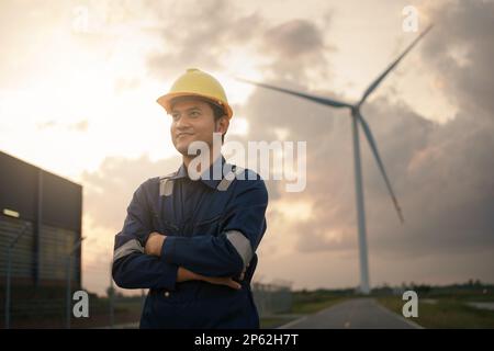 Glücklicher junger Ingenieur in Uniform, der auf dem Feld der Windkraftanlage steht. Stockfoto
