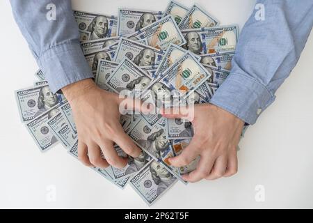 Männerhände und eine Menge Dollarscheine auf einem weißen Holztisch. Bestechung, Korruption, Bargeld. US-Dollar in männlichen Händen. Das Konzept von Profit, Löhnen. Stockfoto