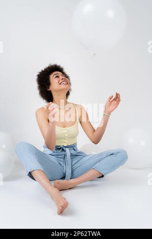 Positive afroamerikanische Frau wirft Ballon auf grauen Hintergrund, Börsenbild Stockfoto