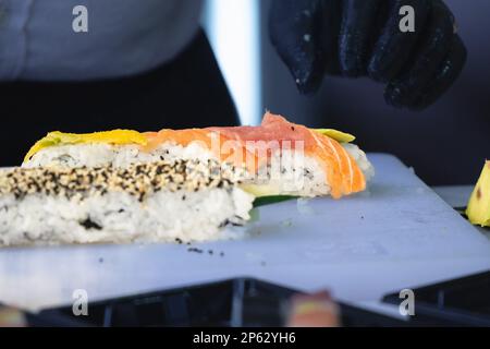 Foto von sushis, wie er vorbereitet und gepackt wird, um geliefert zu werden, mit Fokus auf den Händen eines Sushi-Kochs. Stockfoto