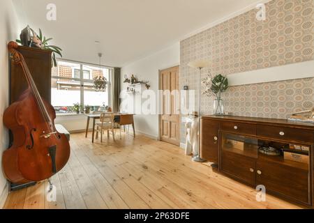 Ein Wohnzimmer mit einem Cello auf dem Boden und einer Tapetenwand im Hintergrund ist ein alter Holzschrank Stockfoto