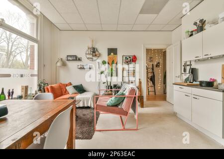 Küche und Wohnzimmer in einem Apartment mit weißen Wänden, Hartholzboden und viel Tageslicht durch die Fenster Stockfoto