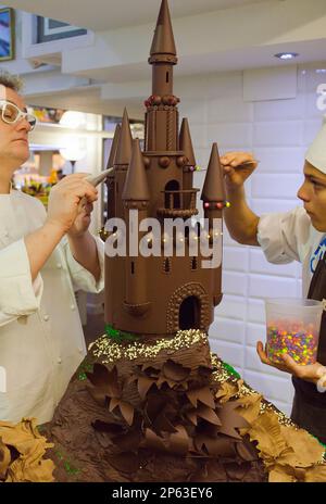 Christian Escriba und eine Assistentin, die einen 'MonaÂ', typischen Schokoladenkuchen von PascuaÂ montag, zubereitet, gibt der Patenonkel seinem Patensohn, der katalanischen Tradition, ESCR Stockfoto