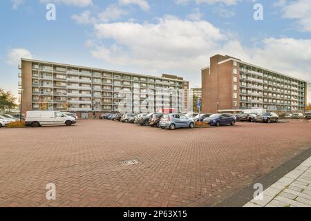 Ein Parkplatz mit Autos parkt auf dem Parkplatz und ein Apartmentgebäude auf der anderen Straßenseite dahinter Stockfoto