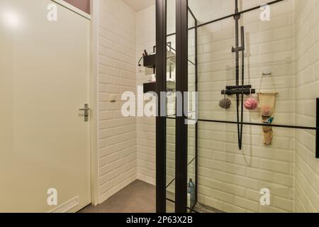 Ein Badezimmer mit weißen Fliesen an den Wänden und schwarzen Zierleisten um die Duschtür, die an der Wand befestigt ist Stockfoto