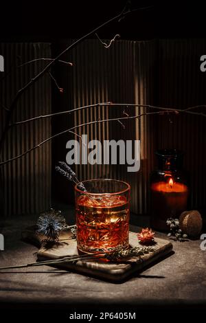 Whisky mit Eis, in einer warmen Umgebung mit Kerze, einigen Blumen und Holz Hintergrund und Tisch, Lavendel und Holz Stockfoto