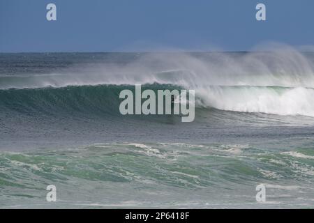 Perfekte Surfwellen Rollen sich in Bells Beach. Ein Surfer taucht bei starkem Wind vor der Küste unter das Wappen der Welle ein, wenn Locken in die Luft gesprüht werden Stockfoto
