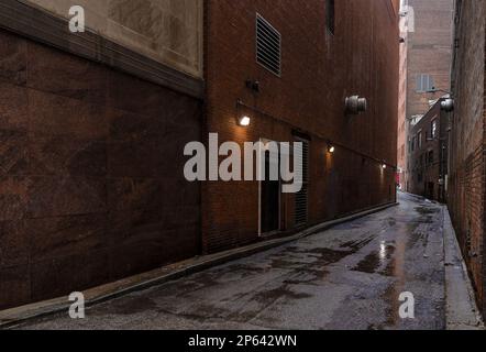 Wasserpfützen auf unebenem Bürgersteig in einer Gasse zwischen Gebäuden in der Innenstadt von Cleveland, Ohio Stockfoto