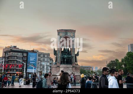 Bild von Taksim Sqaure und Istiklal Straße in der Dämmerung, mit Fokus auf dem Republic Monument, mit Leuten, die davor vorbeigehen. Auch bekannt als Monumen Stockfoto