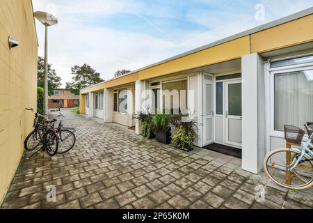 Amsterdam, Niederlande - 10. April 2021: Ein Fahrrad parkt vor einem Gebäude mit Türen und Fenstern auf beiden Seiten, neben einem Fahrrad, das sich gegen die Wand lehnt Stockfoto