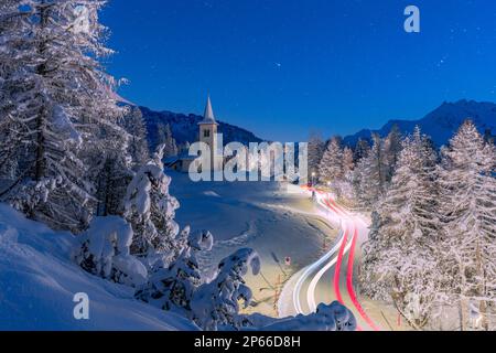 Autospuren Lichter auf der schneebedeckten Bergstraße nach Chiesa Bianca unter den Sternen, Maloja, Engadine, Kanton Graubunden, Schweiz, Europa Stockfoto