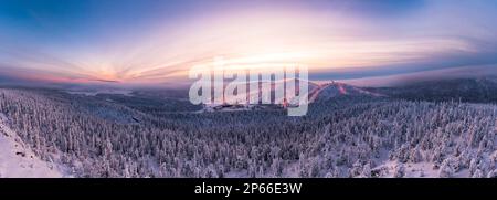 Panoramablick aus der Vogelperspektive auf den verschneiten Wald und die Skipisten unter dem dramatischen Himmel bei Sonnenuntergang, Ruka, Kuusamo, Nordostrobothnia, Lappland, Finnland, Europa Stockfoto