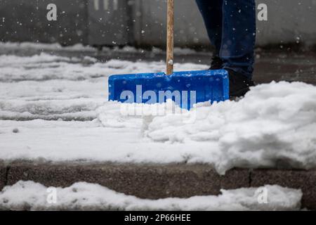 Radevormwald, Deutschland. 07. März 2023. Im Radevormwald im Bergischen Land entfernt ein Mann mit einer Schneeschaufel Schnee vom Bürgersteig. Laut Prognosen des deutschen Wetterdienstes (DWD) wird es am Dienstag überall nass sein: Regen und Graupel dominieren das Wetter. Kredit: Christoph Reichwein/dpa/Alamy Live News Stockfoto