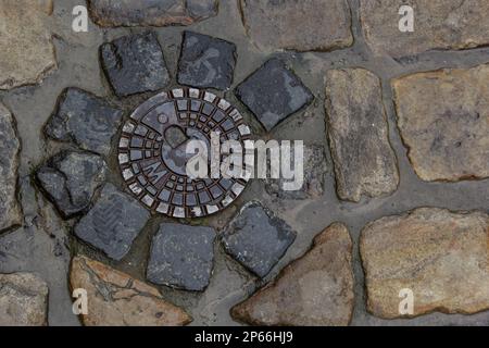 Alte Abwasserluke aus Metall in der Mitte der Straße, aus einem glatten Pflasterstein. Stockfoto