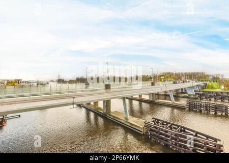 Amsterdam, Niederlande - 10. April 2021: Eine Brücke über das Wasser mit Menschen, die darauf laufen, und Booten im Fluss unten, wie von oben gesehen Stockfoto