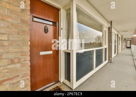 Ein Backsteingebäude mit einer roten Tür und weißen Zierleisten an der Seite des Gebäudes gibt es ein offenes Fenster Stockfoto