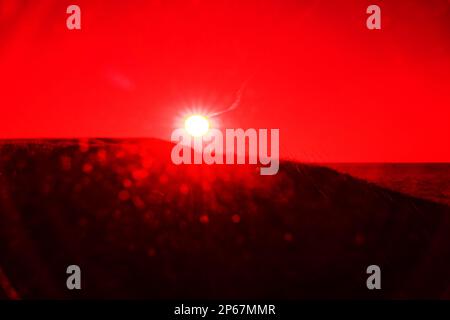 Die Scheibe der untergehenden Sonne mit Sonnenstrahlen und Sonneneruptionen (sog. Pot Protruberance) an der Küste (Hügel und Meer). Surrealistische Kunst Infrarotfotos Stockfoto