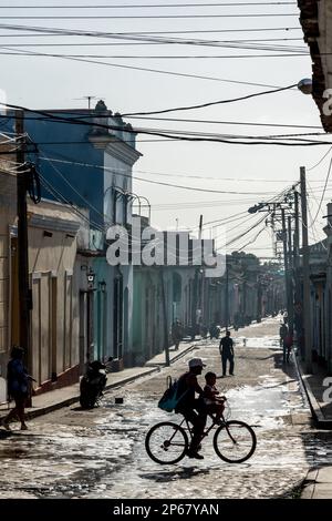 Typische Nebenstraße unter einer Vielzahl von Telefonleitungen, eine Familie mit Silhouetten auf dem Fahrrad, Trinidad, Kuba, Westindischen Inseln, Karibik, Mittelamerika Stockfoto