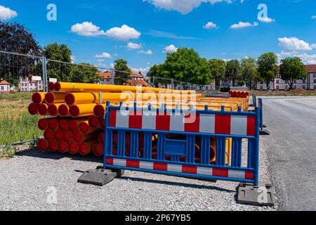 Stapel oranggelber PVC-Leerrohre hinter der tragbaren Kunststoffbarriere. Baustelle in der Stadt. Stockfoto