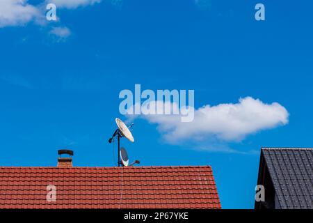 Satellitenschüsseln auf einem gefliesten Dach eines Wohngebäudes. Blauer Himmel mit hellen Wolken. Stockfoto