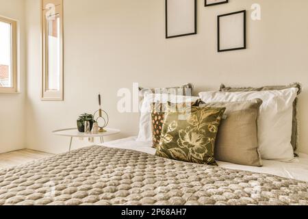 Ein Bett mit Kissen und Bildern an der Wand darüber, in einem Schlafzimmer, das durch Tageslicht gut beleuchtet ist Stockfoto