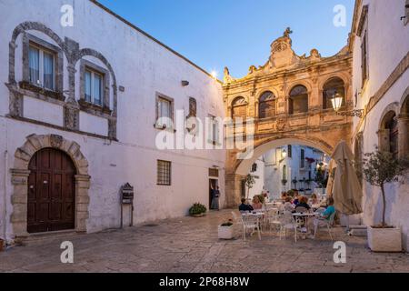 Arco Scoppa Arch und Palazzo Vescovile und Café am Largo Arcid Teodoro Trinchera Platz am Abend, Ostuni, Provinz Brindisi, Apulien, Italien Stockfoto