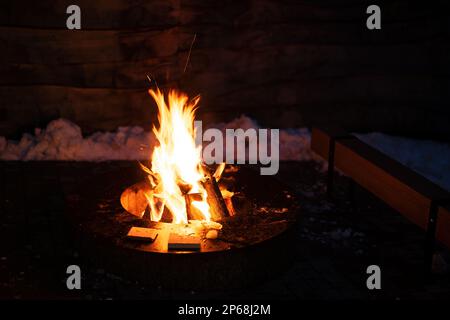 Brennholz brennt in der Mitte eines runden Grilltisches aus Metall. Stockfoto