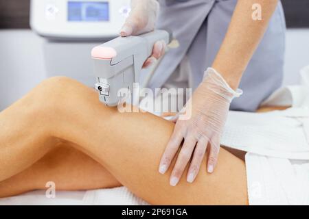 Entspannte junge Kundin, die eine SMAS-Ultraschall-Körperliftmassage mit professioneller Ausrüstung im Beauty Center bekommt. Schließen Stockfoto