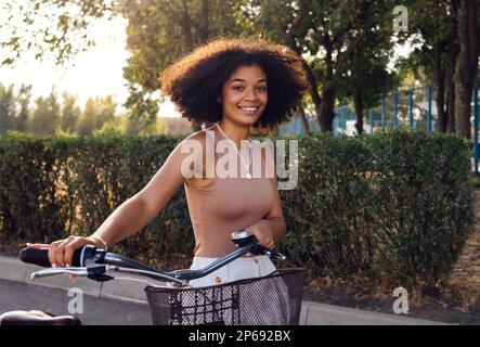 Eine dunkelhäutige Teenagerin fährt ihr Fahrrad. Ein junges und positives afro-amerikanisches Mädchen in lässiger Kleidung lächelt süß und hat Spaß. Stadtstraße an Stockfoto