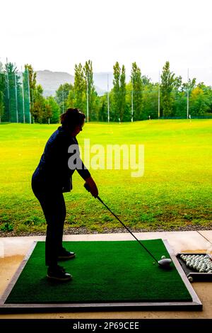 Golferin schult ihren Golf Club Driver an einem Regentag in der Schweiz auf der Driving Range. Stockfoto