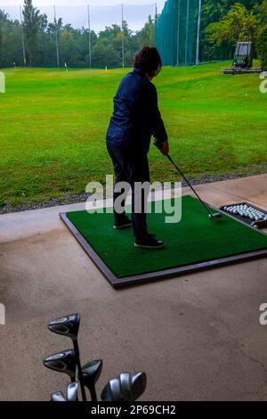 Golferin schult ihren Golf Club Driver an einem Regentag in der Schweiz auf der Driving Range. Stockfoto