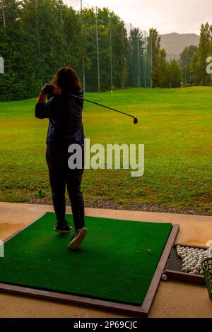 Golferin schult ihren Golf Club Driver an einem Regentag in der Schweiz auf der Driving Range. Stockfoto